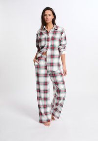 Pidżama w kratę w kolorach białym, czerwonym i zielonym. Koszula z długim rękawem zapinana na guziki, luźne spodnie i miękki materiał.