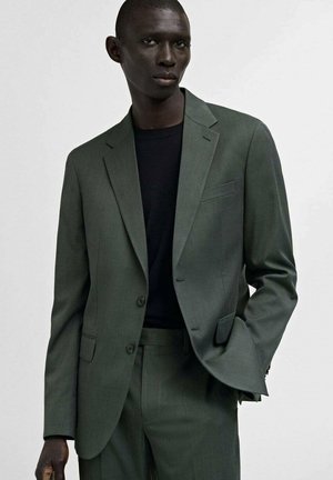 Dark green checkered blazer with notched lapels, two buttons, and front pockets, paired with a black shirt and matching trousers.