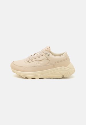 Beige athletic shoes made of smooth synthetic material with a textured rubber sole, featuring round laces and a low-profile design.
