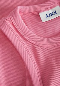 Ružičasti rebrasti top bez rukava s zaobljenim dekolteom i šivenim rubovima. Oznaka "JJXX" vidi se na unutarnjoj strani vrata. Mekana tekstura.
