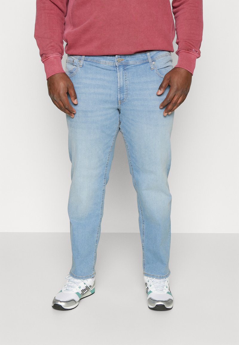 Jeans din denim de un albastru deschis, cu un croi drept, cinci buzunare și închidere cu nasture. Purtați cu o cămașă lungă de culoare maroniu și adidași albi.
