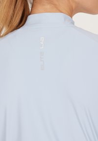 Lichtblauw sportshirt met een hoge kraag, voorzien van een reflecterende witte 'ELITE LAB' logo op de achterkant. Zacht, glad textuur, slim fit.