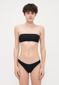 Crni bandeau bikini top s uzorkom mreže, uparen s rubljem niskog struka u odgovarajućem dizajnu. Izrađen od glatkog, rastezljivog materijala.