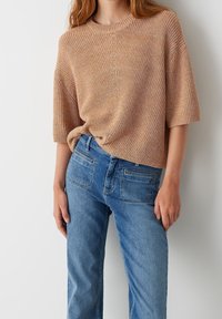 Beżowy sweter dzianinowy z krótkimi rękawami, luźny krój, teksturowany wzór, okrągły dekolt. Połączony z jasnoniebieskimi dżinsami z kieszeniami.