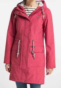 Kvinde iført en lyserød hætte-regnjakke med hvid og sort snore, forlommer og en stribet skjorte under.