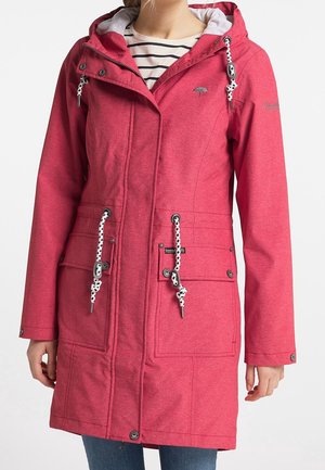 Femme portant un imperméable à capuche rose avec des cordons de serrage blancs et noirs, des poches avant et une chemise rayée en dessous.