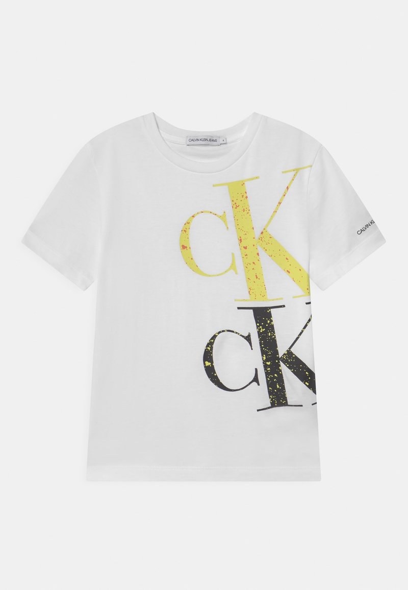 Hvid T-shirt med korte ærmer, der har store overlappende gule og sorte "cK" bogstaver og et lille Calvin Klein-logo på venstre ærme.