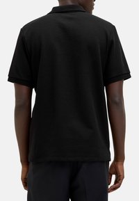 Sort polo shirt med korte ærmer, et tekstureret stof og en klassisk krave. Kanten er let buet med en subtil kontrastkant.