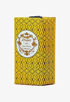 L'emballage du savon Lavande présente un design jaune vif avec des motifs noirs élaborés. Une étiquette blanche affiche le nom du produit et la marque.