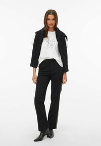 Črne hlače z visokim pasom in belimi črtami ob strani, kombinirane z belim majico z ilustracijo obraza v risbi iz ene črte, slojeno s črnim puloverjem.