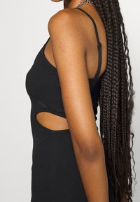 Robe débardeur noire côtelée avec une découpe sur le côté, bretelles fines ajustables et silhouette ajustée. Tissu texturé.