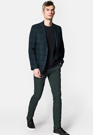 Męska marynarka w ciemnozieloną kratę, połączona z czarną koszulą, zielonymi spodniami slim-fit oraz czarnymi trampkami z białymi podeszwami.