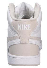 Sneaker Nike con una toma in pelle bianca texturizzata e accenti beige chiaro. Presenta un colletto imbottito e il logo 'NIKE' sul tallone.