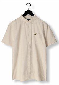 Camisa de botones de manga corta beige con cuello, bolsillo en el pecho y pequeño logo de un pájaro amarillo, colgada en una percha negra contra un fondo blanco.