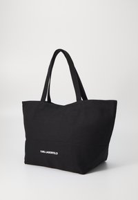 Fekete vászontáska két strapabíró füllel, a fronthoz fehér "KARL LAGERFELD" logóval és tágas, nyitott kialakítással.