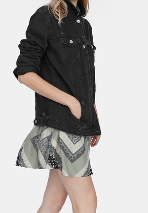 Person trägt eine schwarze Denimjacke mit hochgekrempelten Ärmeln und einen gemusterten, ausgestellten Rock mit grauen und schwarzen Designs.
