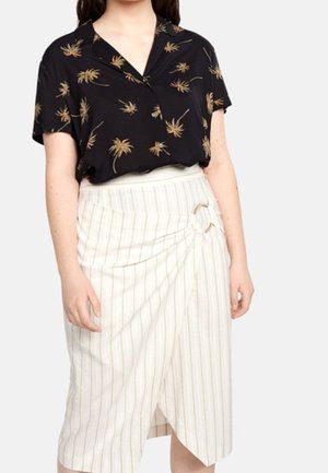 Femme portant une chemise noire à manches courtes avec imprimé floral et une jupe portefeuille blanche à fines rayures avec une boucle latérale.