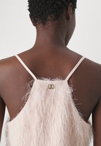 Abito rosa chiaro con una texture pelosa, dotato di sottili spalline regolabili e un dettaglio in oro sulla schiena.