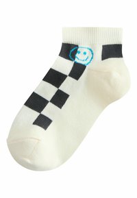 Chaussette blanche à la cheville avec un motif à carreaux noirs sur le côté et un petit visage souriant bleu près du bord-côte.