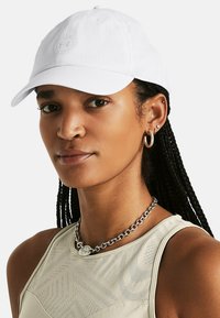 Gorra de béisbol blanca con visera curva y tejido texturizado. Presenta un parche con un logo central y detalles de costura.