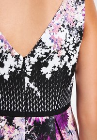 Blumendruckkleid mit schwarzem Oberteil und V-Ausschnitt, strukturiertem Stoff und einem Rock mit lila Blumenmuster.