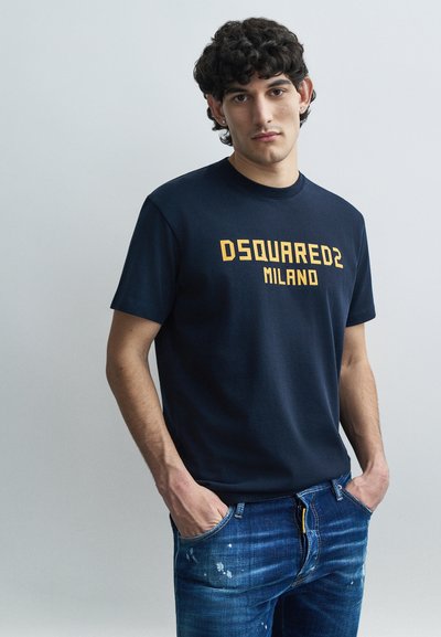 Marineblaue Baumwoll-T-Shirt mit gelbem "DSQUARED2 MILANO"-Schriftzug auf der Vorderseite; kurze Ärmel und Rundhalsausschnitt. Blaue, abgenutzte Denim-Jeans.