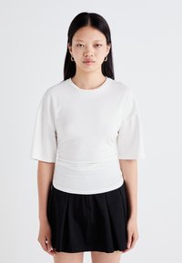 Witte, kortekorte top met een geplooid ontwerp bij de taille, gecombineerd met een zwarte geplooide rok. Glad textuur, ronde halslijn.