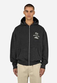 Černá mikina na zip vyrobená z bavlny, s velkou přední kapsou, žebrovanými manžetami a vyšitým designem na levé části hrudi.