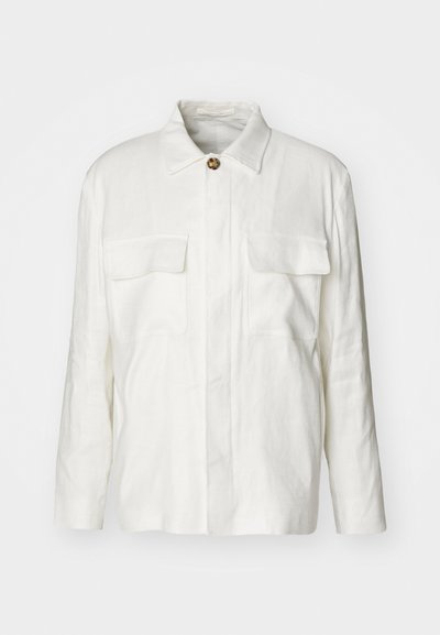 Λευκό λινό πουκάμισο με κολάρο, κουμπιά μπροστά και δύο τσέπες στο στήθος. Διαθέτει μακριά μανίκια και χαλαρή εφαρμογή.