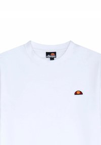 Biała bawełniana koszulka z okrągłym dekoltem. Posiada małe, wyszywane logo w kolorze pomarańczowym i czerwonym umiejscowione po lewej stronie na klatce piersiowej.