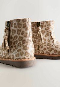 Stivaletti alla leopardata con una superficie morbida e texture, dotati di dettagli con nappine e una cerniera laterale, su una suola marrone resistente.
