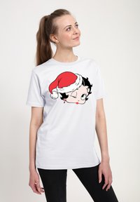 Hvid bomuld t-shirt med et grafisk motiv af en karakter, der blinker og bærer en rød nissehat, med sort hår og grønne øjne, trykt i sort og rød.