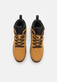 Botas de cuero marrón hasta el tobillo con acentos negros, punta redonda y cordones negros. Cuentan con una lengüeta en el talón y suelas de goma.
