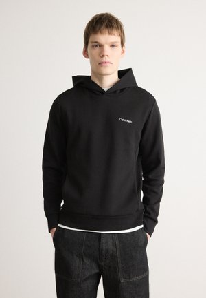Black hooded sweatshirt with a front pocket, made of soft fabric, features a small white "Calvin Klein" logo on the chest.
