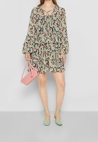 Blumenkleid mit langen Ärmeln und gestuften Rüschen in Grün, Pink und Schwarz. Kombiniert mit einer pinken Handtasche und mintgrünen Schnürflats.