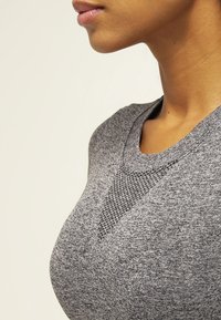 Top atlético gris con cuello redondo, detalle texturizado en el pecho y mangas cortas; hecho de una tela suave y elástica.
