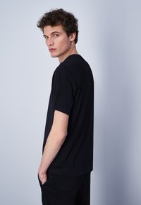 Camiseta de algodón negra con un corte relajado, mangas cortas y cuello redondo, vista de perfil sobre un fondo claro.