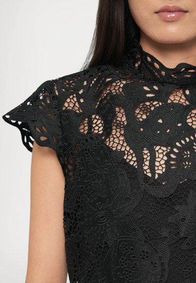 Czarna koronkowa bluzka z motywami kwiatowymi i geometrycznymi, z falistymi krótkimi rękawkami, wysokim dekoltem i misterną fakturą.