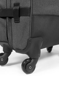 Šedý kufr s textilním povrchem, černým plastovým dnem a čtyřmi gumovými kolečky pro snadnou manipulaci. Obsahuje popruh pro bezpečné uchopení.