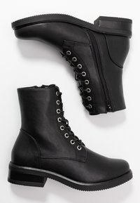Černé kožené kotníkové boty s šněrováním v přední části, stříbrné očka, boční zip a plná gumová podrážka. Hladký povrch, design s kulatou špičkou.
