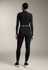 Fekete, testhezálló, hosszú ujjú crop top és magas derekú leggings, sima anyagból készült. A szettet fekete, fehér talpú sportcipők egészítik ki.