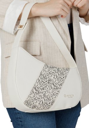 Hvid skuldertaske i halvmåneform med sort og hvidt tekstureret midterpanel båret over beige blazer og blå jeans.