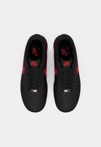Black Nike Air Force 1 sneakers with red accents, featuring round laces, perforated toe, and logo on tongue. Smooth synthetic material.