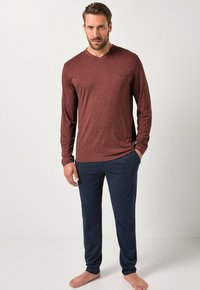 Top de manga larga color burdeos con cuello en v y bolsillo en el pecho, combinado con pantalones de canalé azul marino. El conjunto es informal y está hecho de un tejido suave.