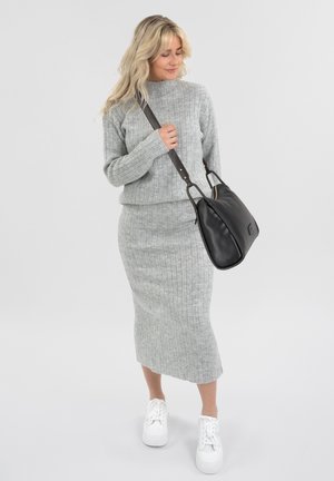 Maglione grigio a costine e gonna midi coordinata con una silhouette aderente. Borsa a tracolla nera con manico e sneakers bianche.