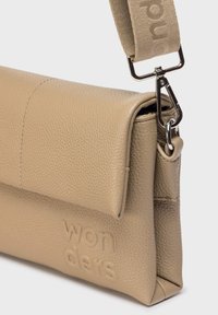 Beżowa skórzana torba na ramię z teksturą, z klapą, odpinanym materiałowym paskiem, metalowym zapięciem oraz wytłoczonym logo "wonders" z przodu.