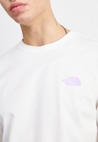 Bílý bavlněný tričko s malým fialovým logem "The North Face" na levé části hrudi. Kulatý výstřih a krátké rukávy.