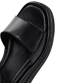 Infradito in pelle nera con una larga fascia, texture liscia, forma sagomata e suola spessa per comfort e supporto.
