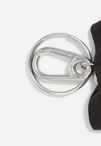 Moschettone in metallo con finitura argentata lucida collegato a un anello circolare, accompagnato da un nastro di stoffa nera.