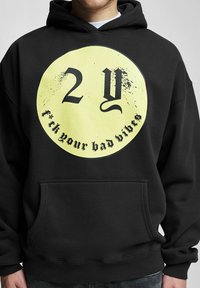 Fekete kapucnis pulóver, amelyen egy nagy sárga körgrafika található az "2Y" számokkal és a "F*ck your bad vibes" felirattal vastag fekete betűkkel. Kenguruzsebkészítmény.